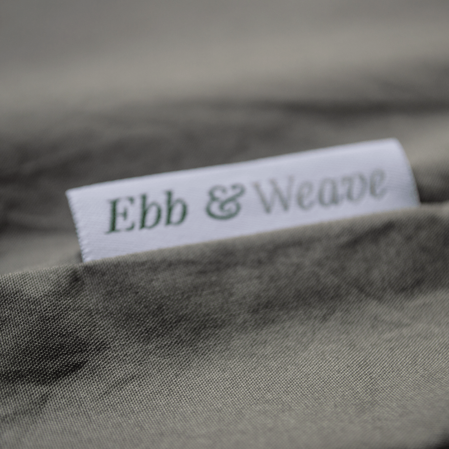 A macro image of a cotton grey bedding set showing the beautiful percale pattern and the Ebb and Weave label